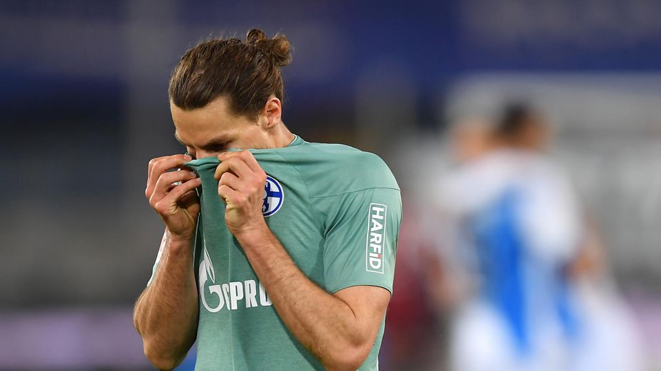 Ein Fußballer mit braunem Zopf verbirgt sein Gesicht im kupfergrünen Schalke-Trikot